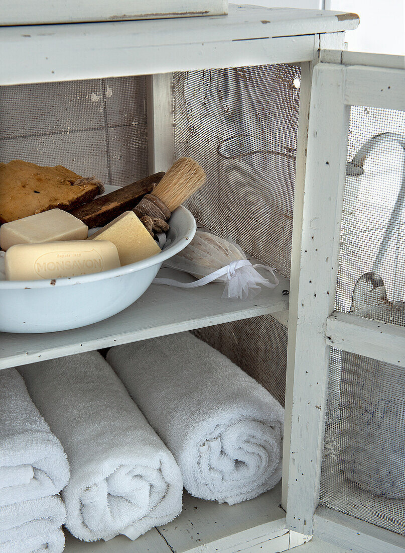 White wooden cabinet with towels and soaps in a tin bowl