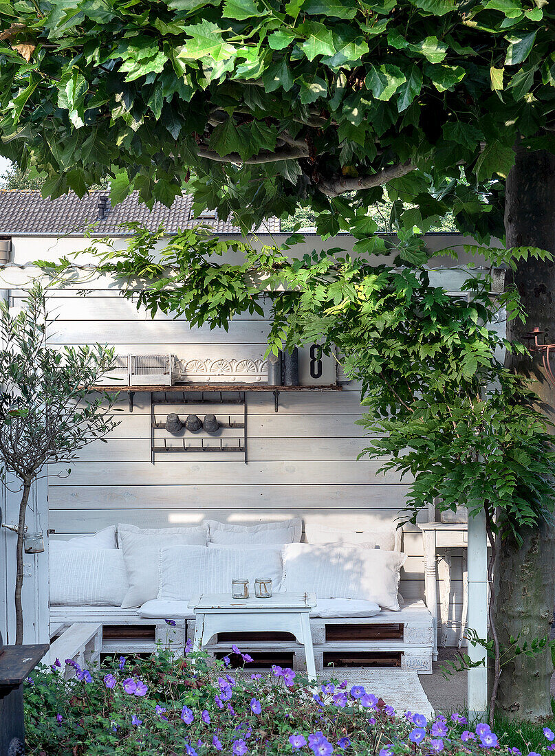 White seating area made of pallets on terrace, surrounded by plants