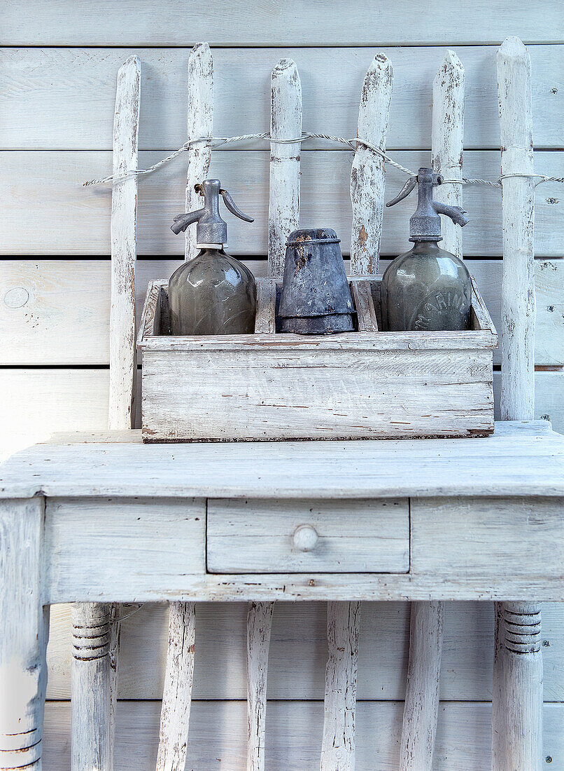 Vintage siphon bottles and metal jug on a wooden table in front of a white-painted wooden wall