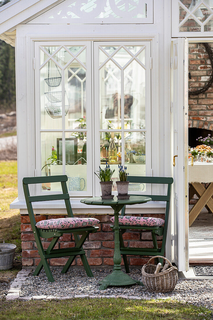 Cosy seating area with green metal table and chairs in front of greenhouse