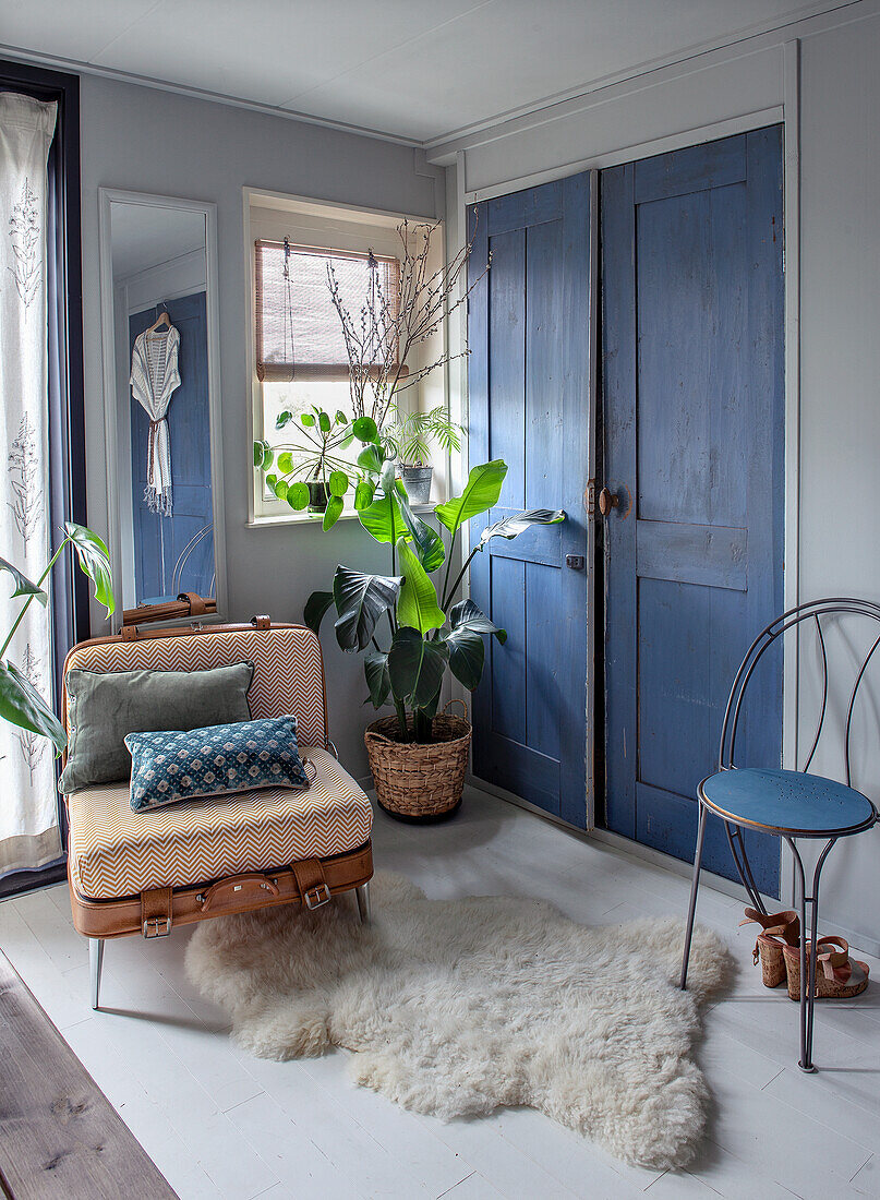 Vintage-Koffersessel, blauer Holzstuhl und Lammfell im Schlafzimmer