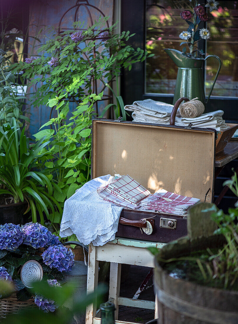 Open suitcase with lace and linen cloths in a rustic garden