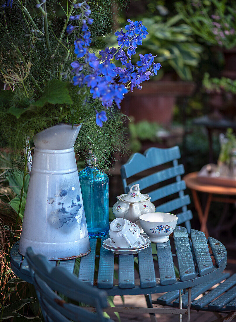 Blauer Gartentisch mit Teeservice und blauem Rittersporn (Delphinium) in Kanne