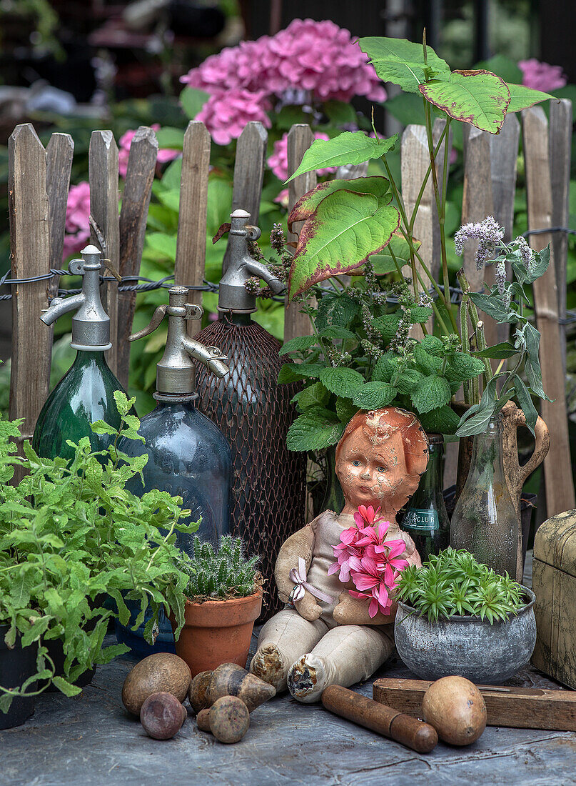 Nostalgische Gartendekoration mit alten Siphonflaschen und einer antiken Puppe