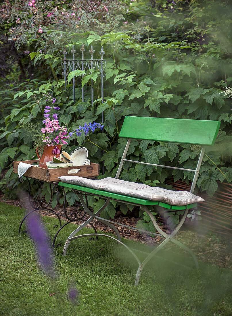 Green garden bench with cushions and wooden tray with flower arrangement