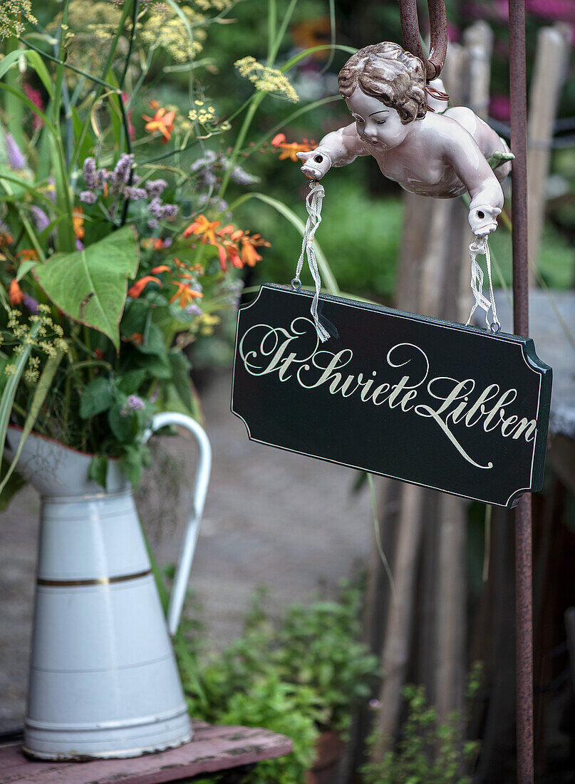 Garten-Dekoration: Blumenstrauß in Kanne und Engelsfigur mit Schild "It Swiete Libben"