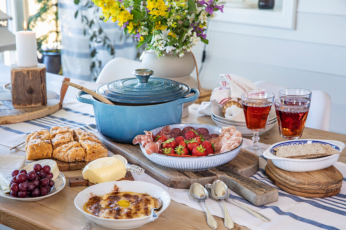 Reichlich gedeckter Frühstückstisch mit Obst, Gebäck und blauem Bräter