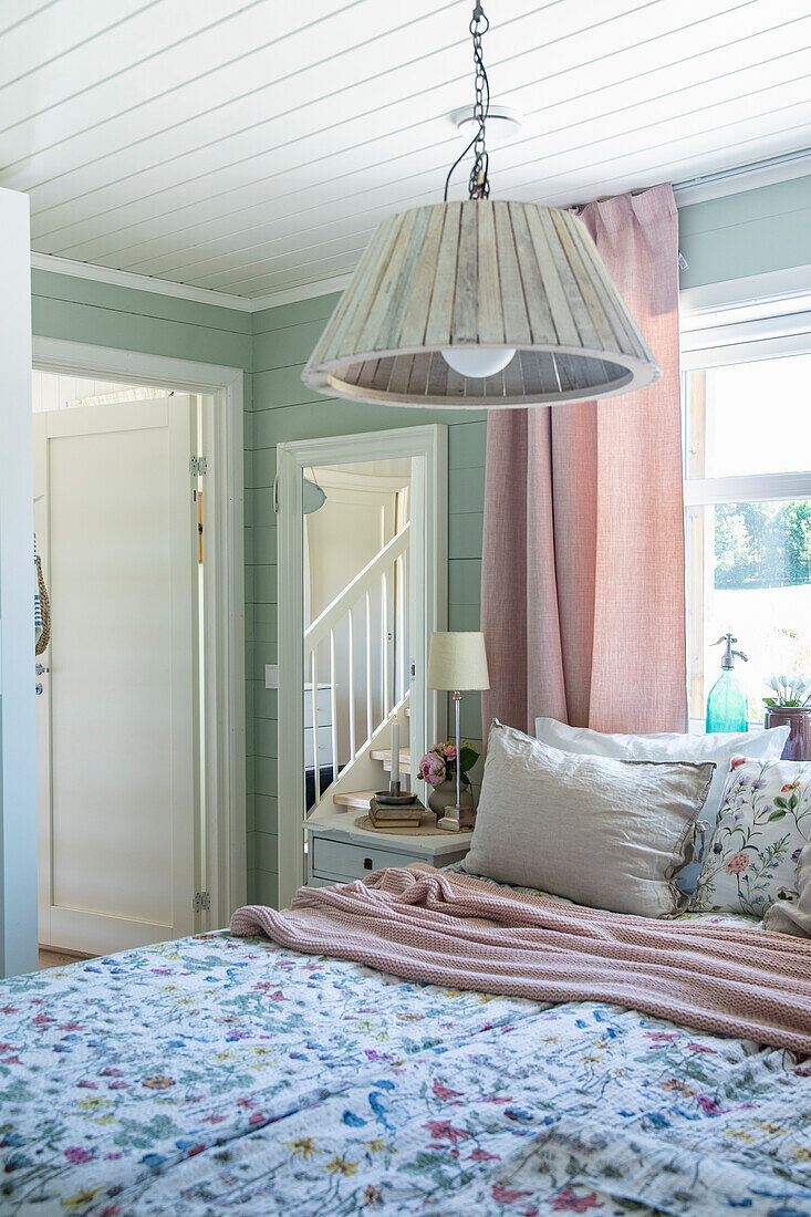 Bedroom with pastel green walls, floral bed linen and wooden lamp