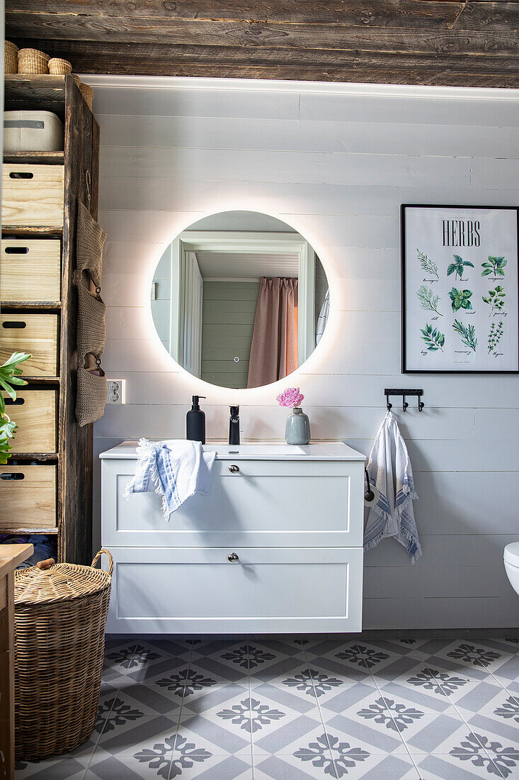 Bathroom with white cabinets, illuminated round mirror and patterned floor tiles