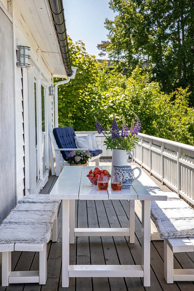 Gedeckter Holztisch mit Erdbeeren, Erfrischungsgetränk und Lupinen-Strauß auf der Terrasse