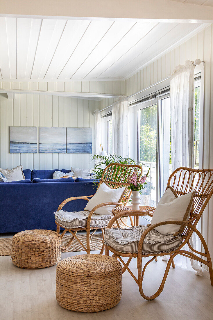 Living room with wicker armchairs and blue corner sofa in front of large windows