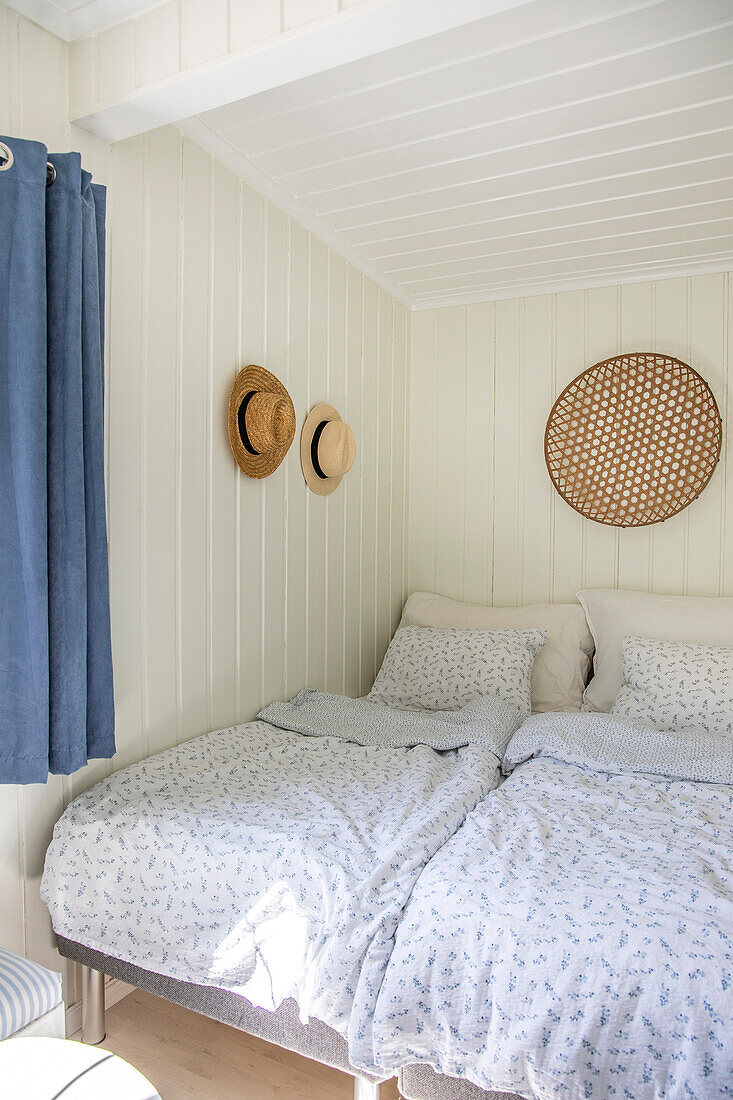 Bedroom with white wood paneling and straw hats on the wall