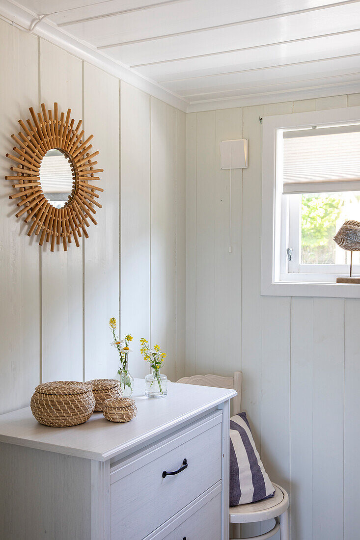 Wood-paneled room with chest of drawers, wall mirror and decoration made from natural materials