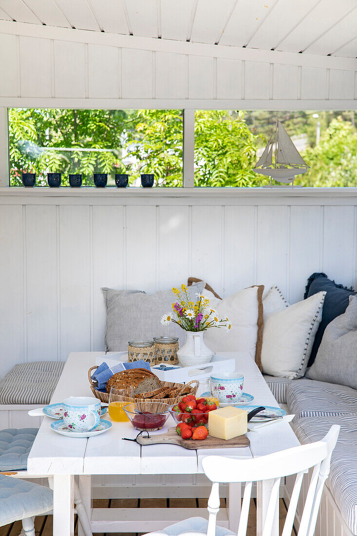 Gedeckter Esstisch mit Frühstück und Blumenstrauß auf einer hellen Veranda