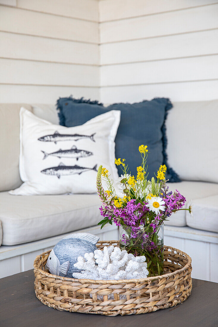 Rattan-Tablett mit Blumenstrauß und maritimer Dekoration vor Sitzbank