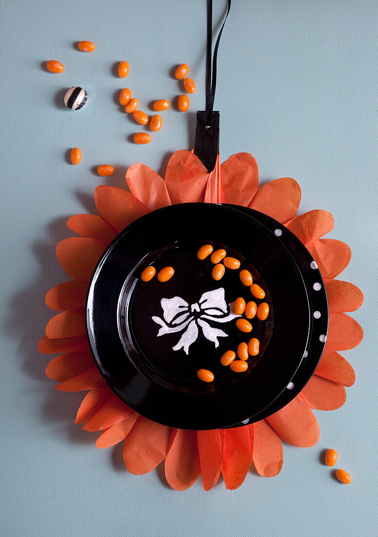 Black plate with bow motif and orange-coloured sweets on a decorative paper flower background