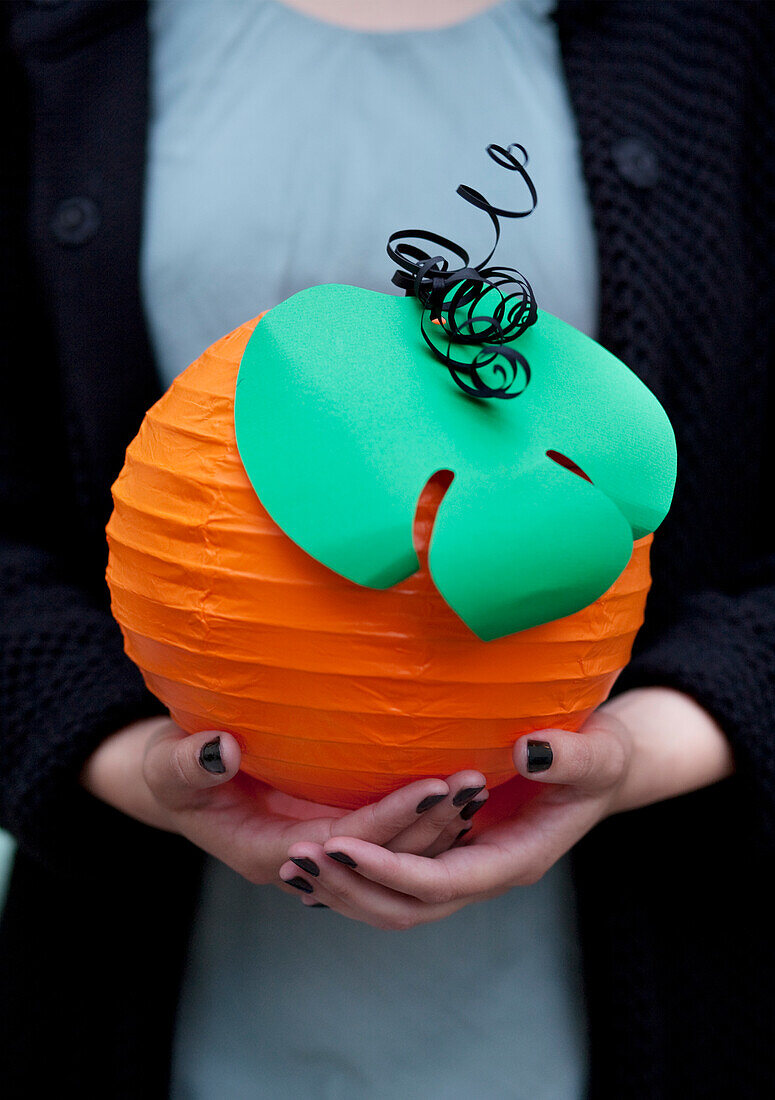 Hands holding a pumpkin-shaped paper lantern