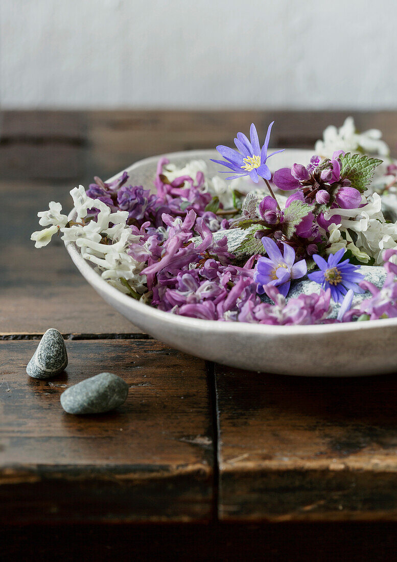 Schale mit bunten Frühlingsblumen auf rustikalem Holztisch