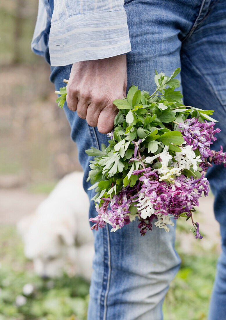 Frauenhand hält Frühlingsblumenstrauß im Garten