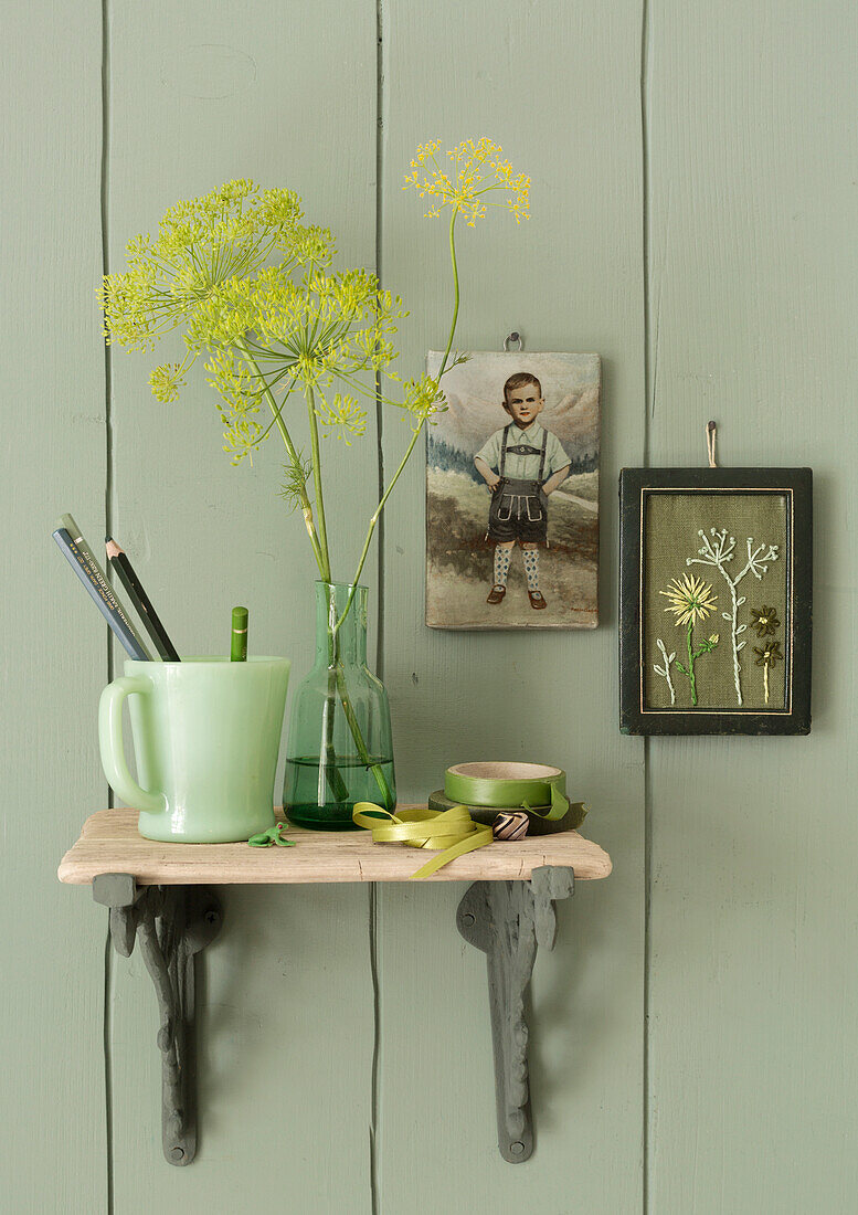 Decorated, small wall shelf with green vase, pencil cup and embroidery pictures