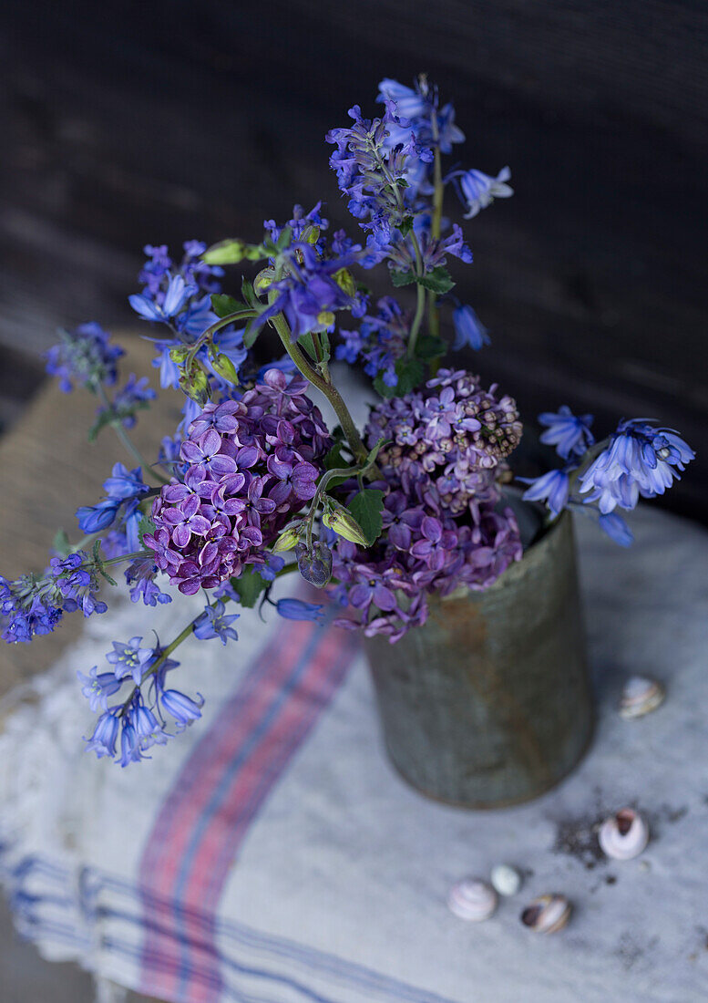 Bouquet of blue and purple flowers in tin vase on table