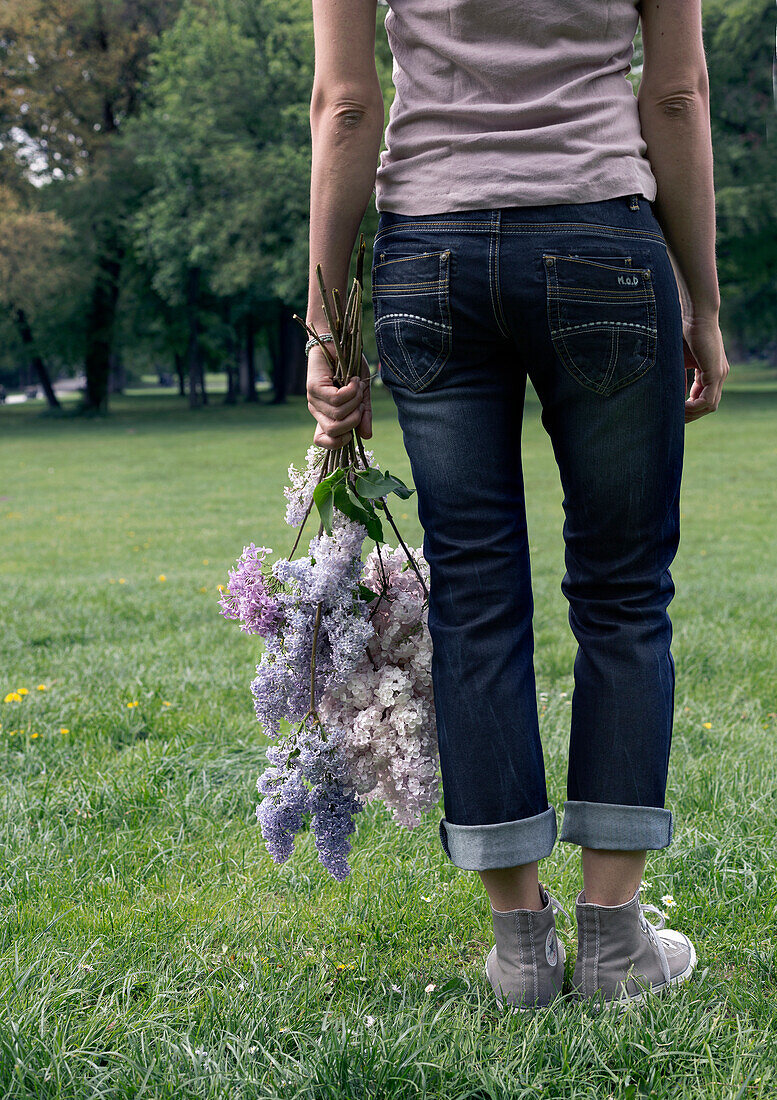 Person mit einem Strauß aus Flieder (Syringa) auf einer Wiese im Park