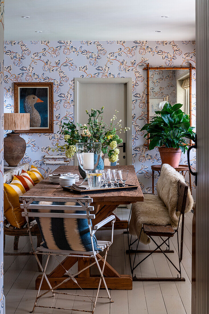 Dining room with rustic wooden table, floral arrangement and patterned wallpaper