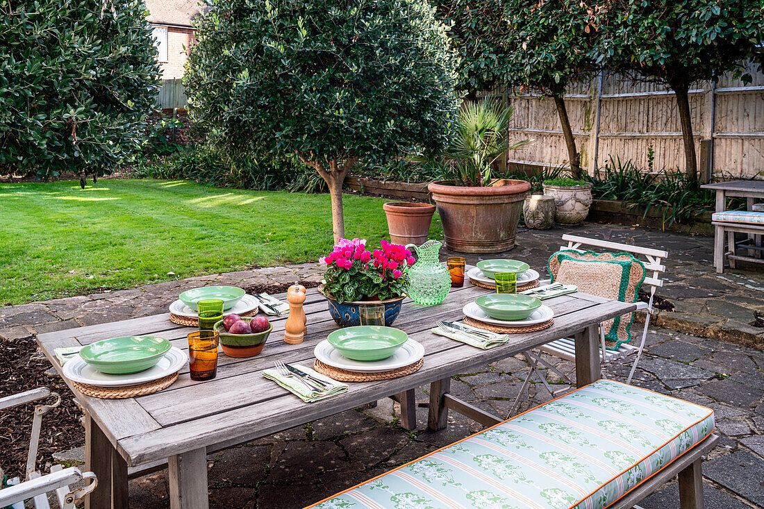 Gedeckter Holztisch im Garten mit Blumentopf und Geschirr in Grüntönen