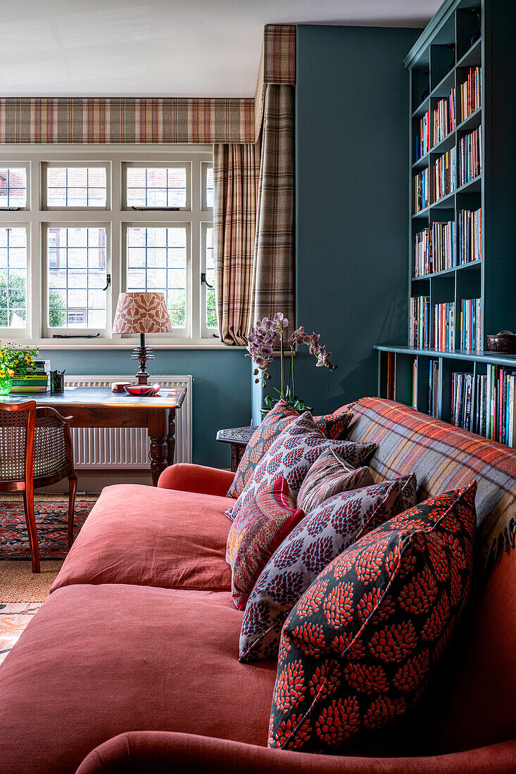 Living room with red sofa, patterned cushions and bookshelf in front of window front