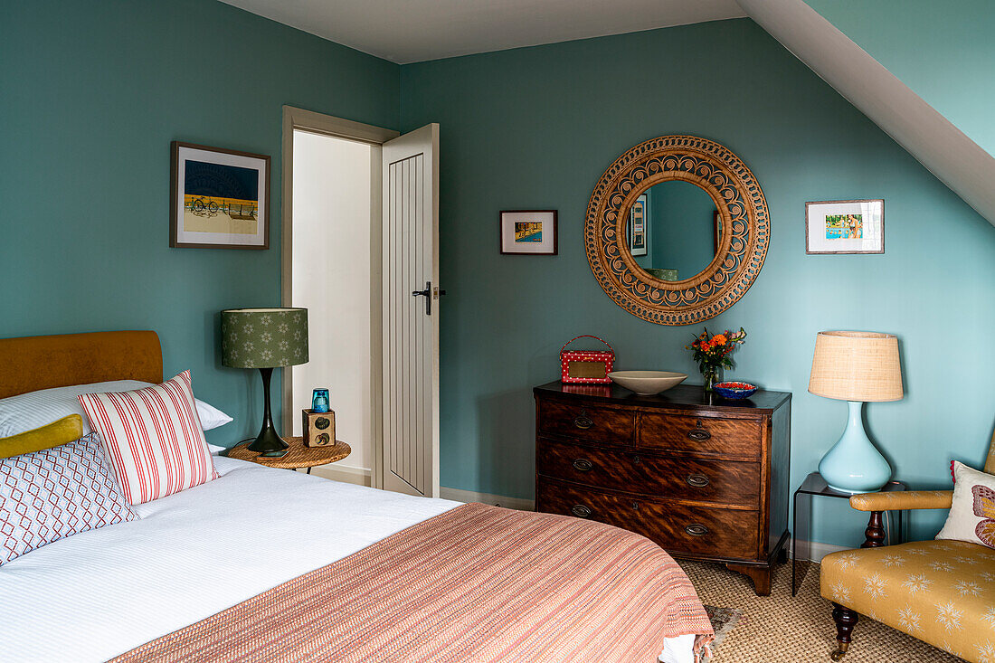 Bedroom with wooden furniture, round wall mirror and green-blue colored walls