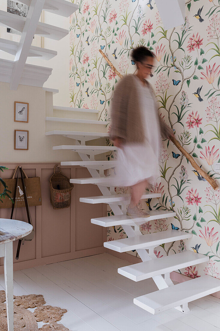 Frau auf weißer Wendeltreppe mit floraler Tapete und hellen Holzakzenten