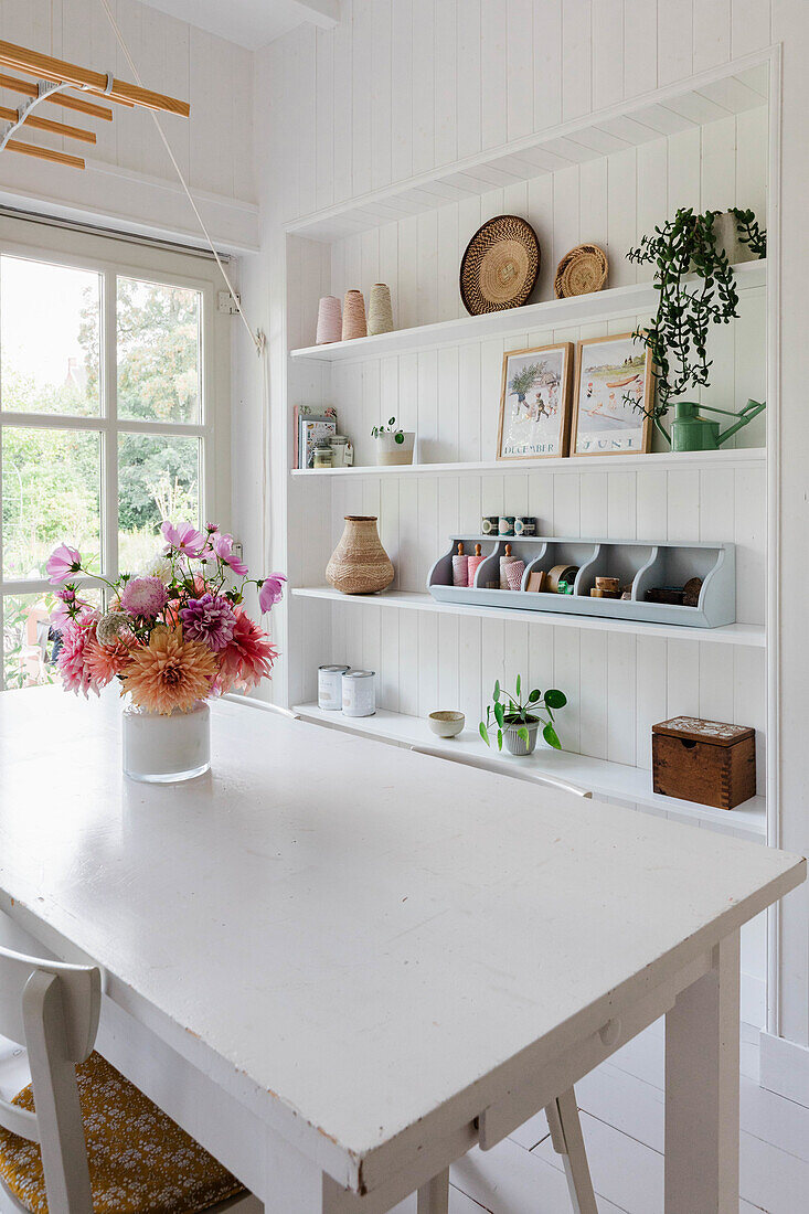 White dining area with wall shelves and bouquet of flowers on table