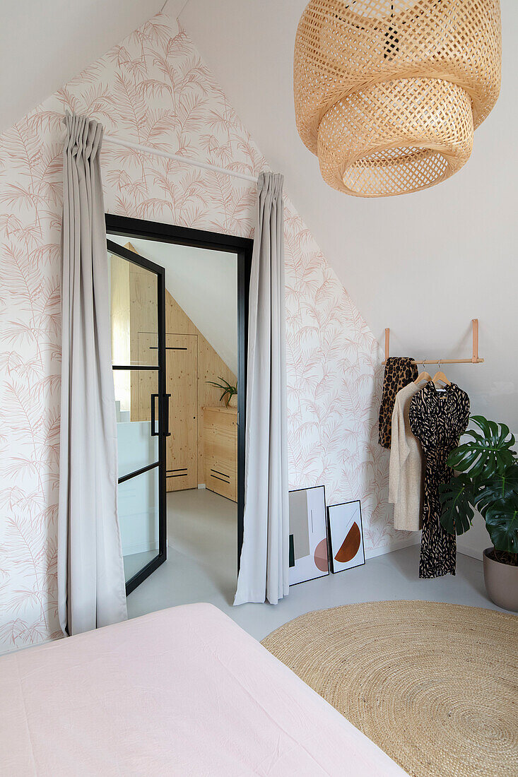 Attic bedroom with patterned wallpaper, rattan hanging lamp and black glass door frame