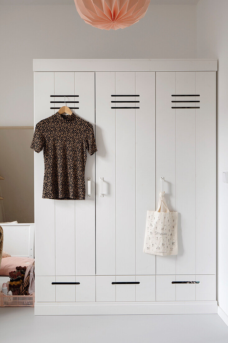 Weißer Kleiderschrank mit hängendem T-Shirt und Jutetasche im Schlafzimmer