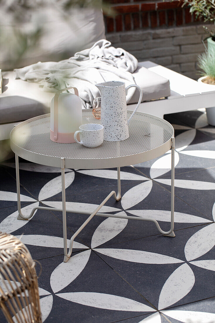 Round metal table with jug and cup on tiled terrace