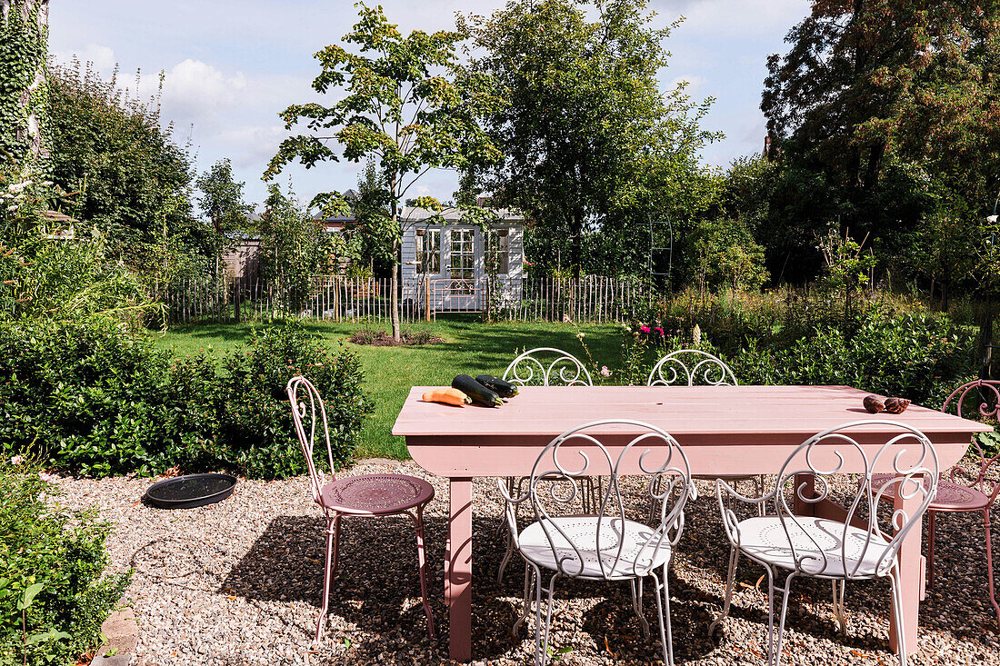 Gartentisch mit weißen und rosa Stühlen auf Kiesfläche im sommerlichen Garten