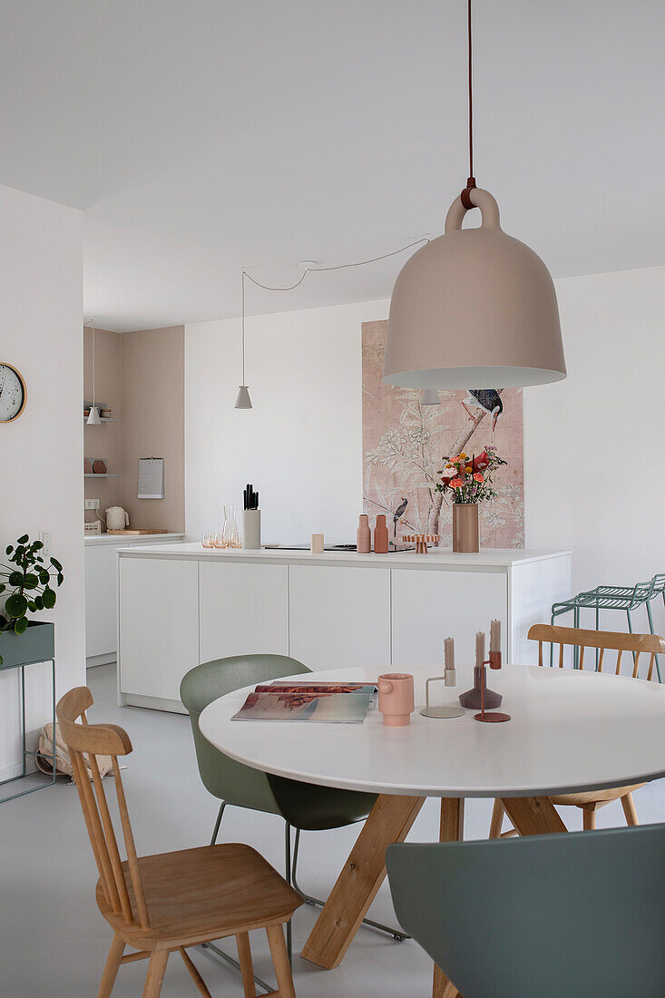 Dining area with white round table, various chairs and pink hanging lamp in a modern kitchen