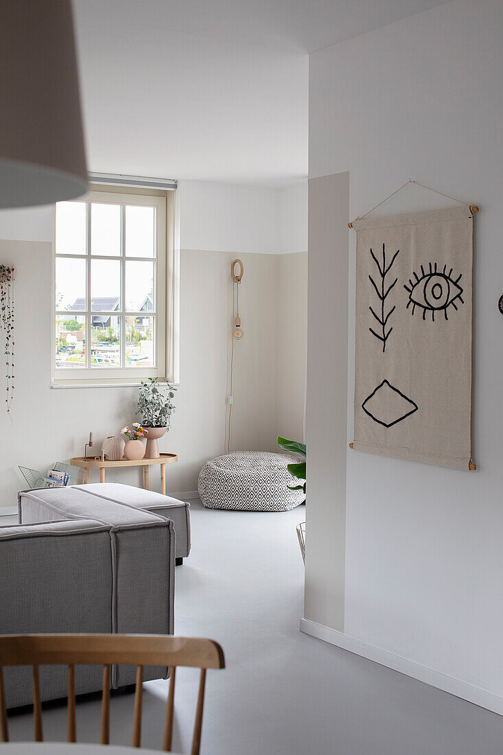 Open-plan living room with grey sofa, pouf and abstract tapestry