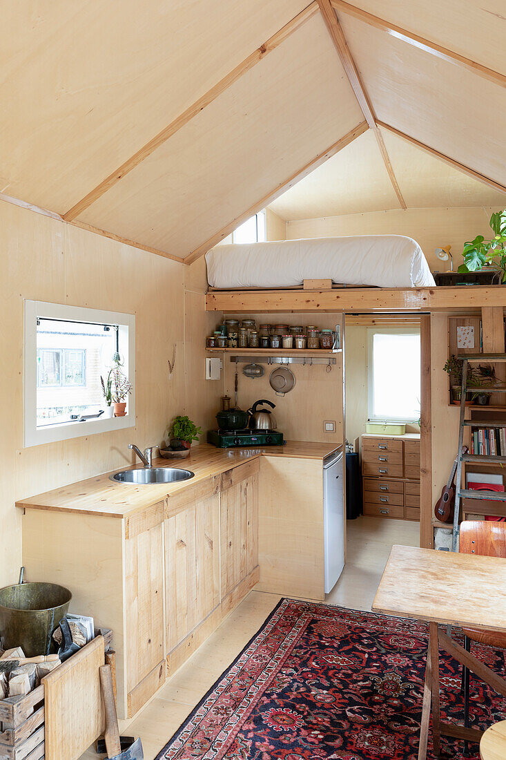 Small kitchen with wooden panelling and sleeping area in a tiny house