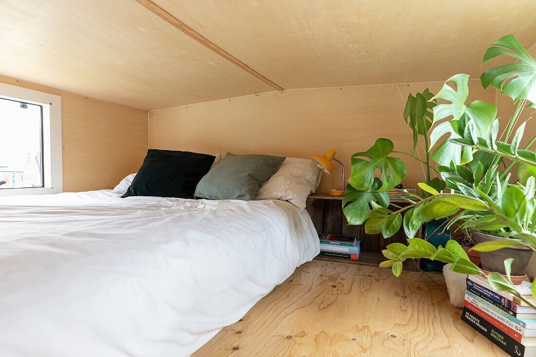 Kleines Schlafzimmer mit niedriger Decke, Bücherstapel und Monstera-Pflanze