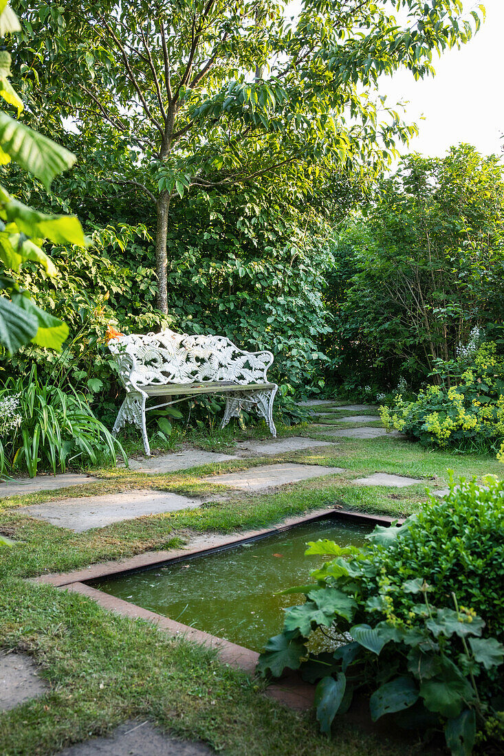 Romantic garden bench with small pond and natural stone path