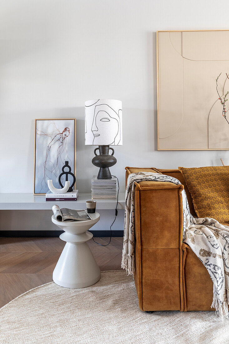 Living room with cognac-coloured sofa, abstract wall paintings and modern side table