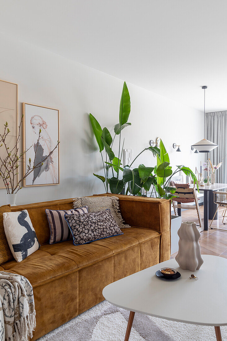 Living room with mustard yellow velvet sofa, large-leaved houseplants and modern artwork on the wall