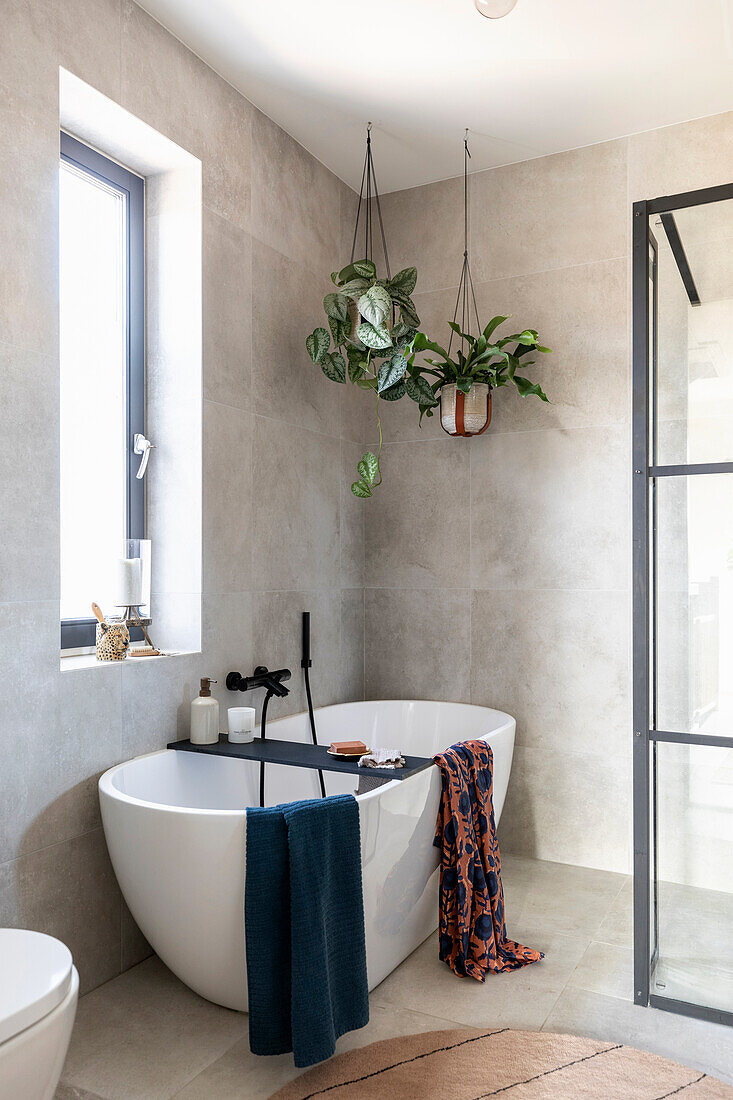 Free-standing bathtub with hanging plants and colourful towels in a modern bathroom