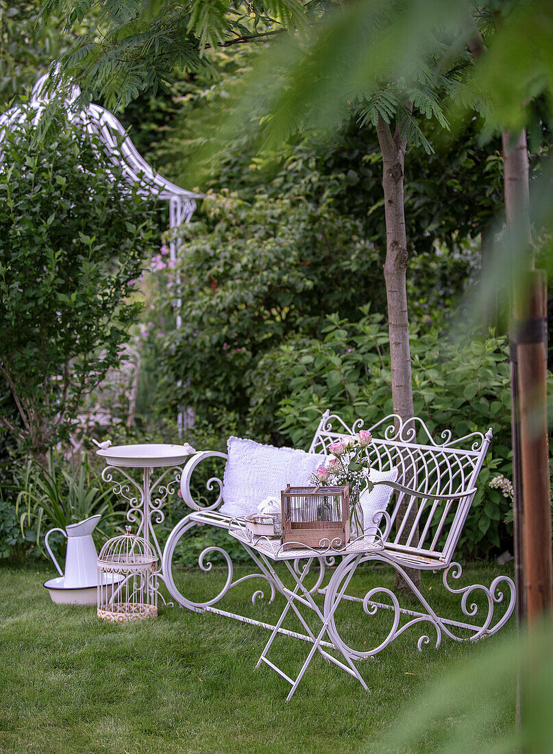 Nostalgic garden bench with lace cushions and bird bath in a romantic garden