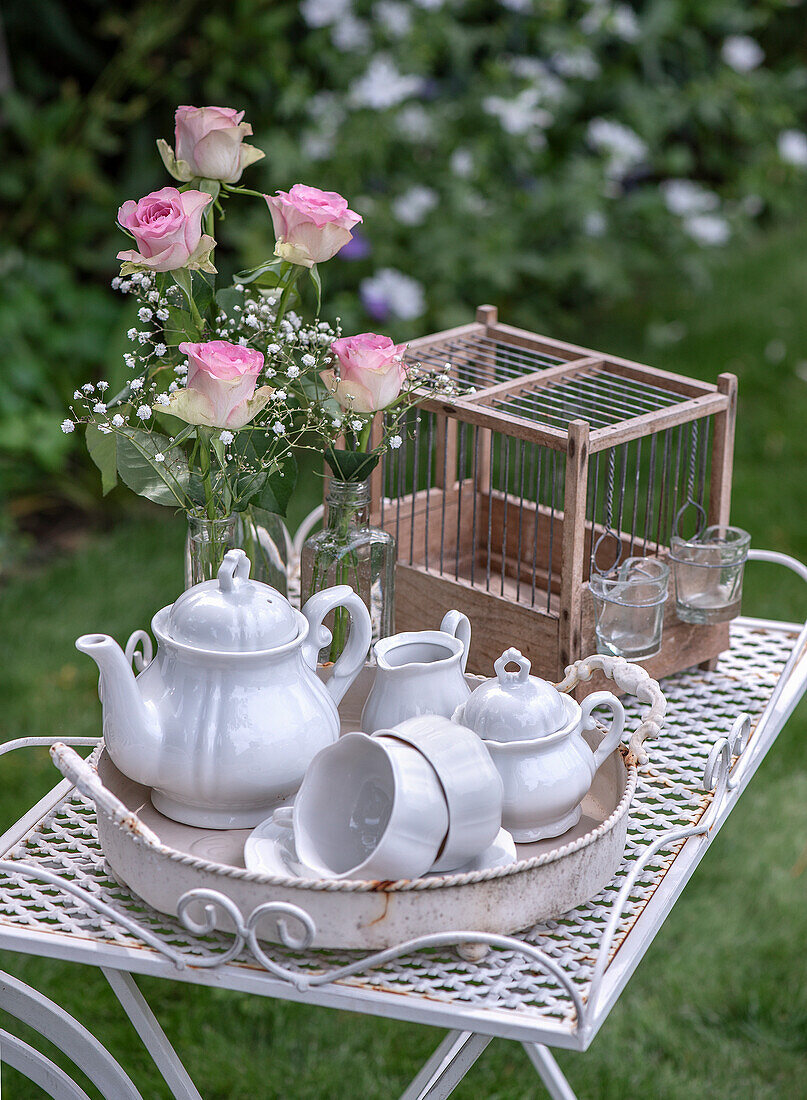 White tea service with pink roses on a rusty garden table