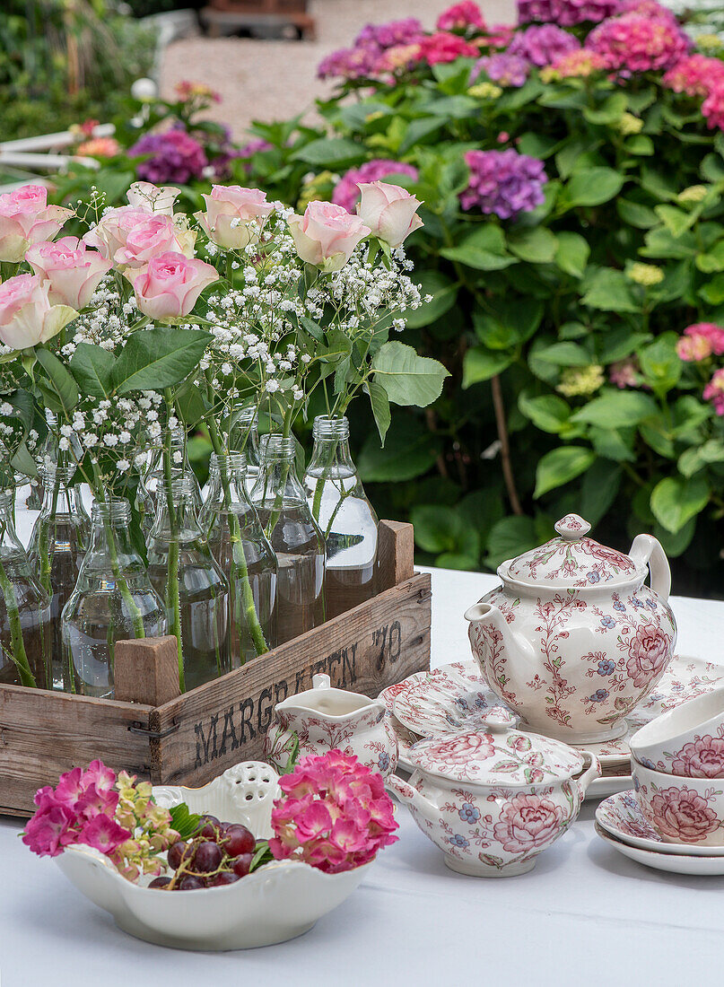 Vintage tea service with bouquets of roses and hydrangeas on a garden table