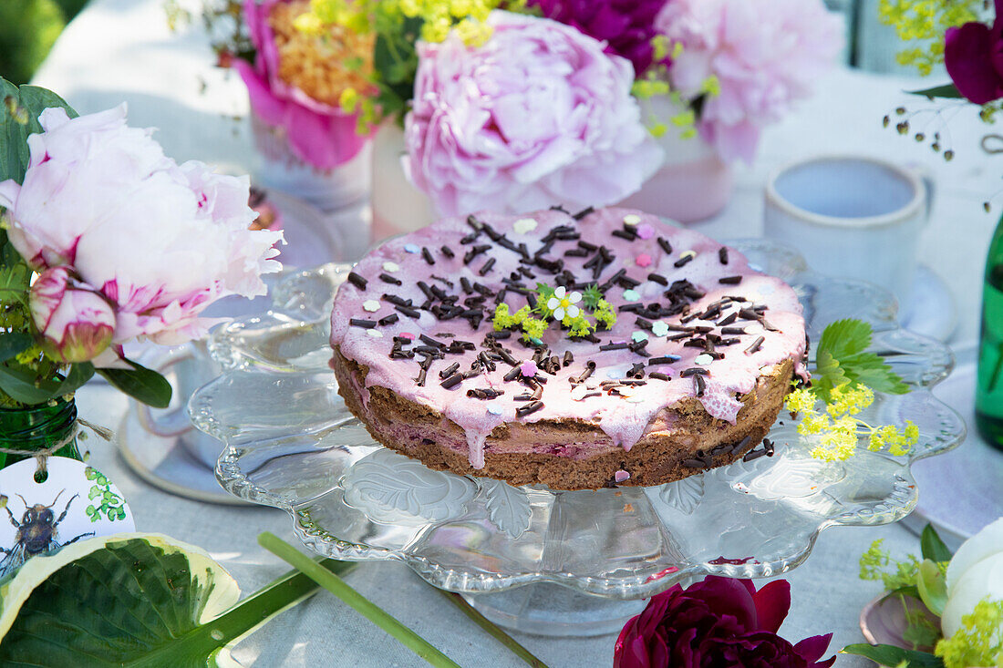 Gedeckte Tafel mit Schokoladenkuchen und Blütenbouquet aus Pfingstrosen