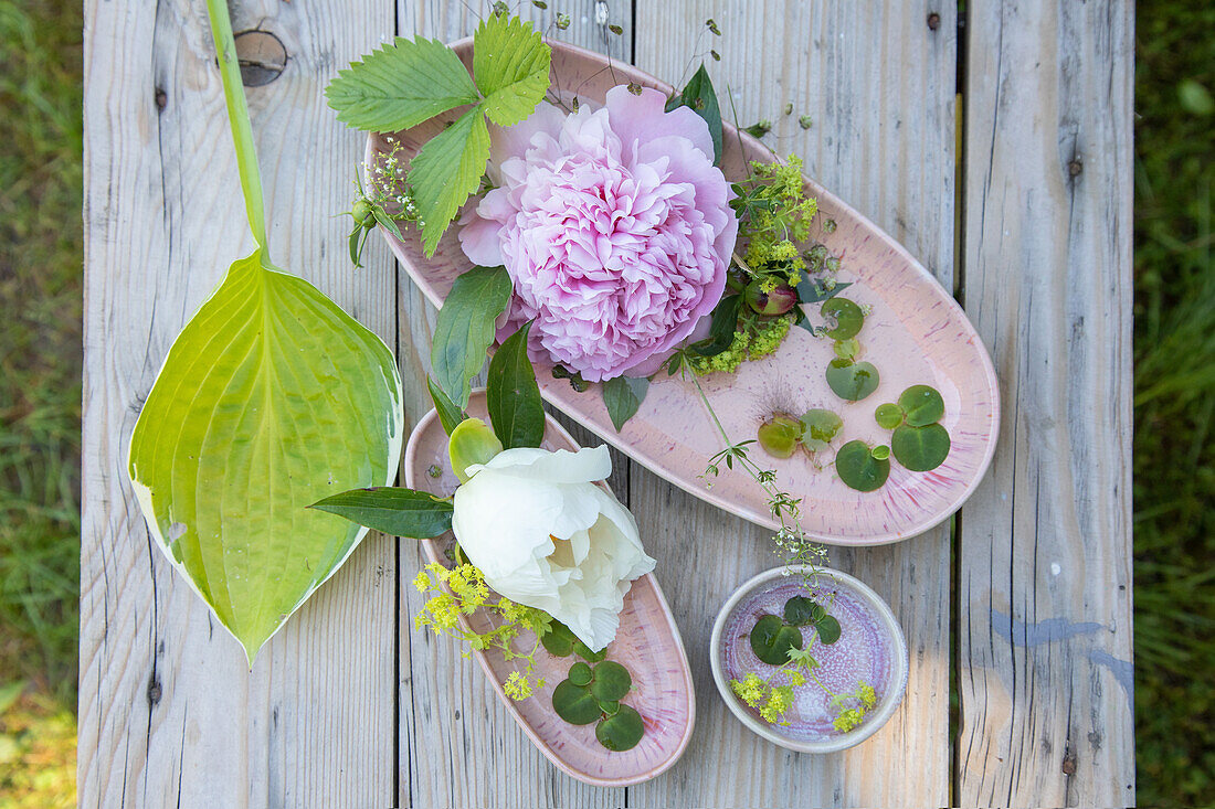 Blumenarrangement mit Pfingstrosen (Paeonia) und Hostablatt auf Holztisch