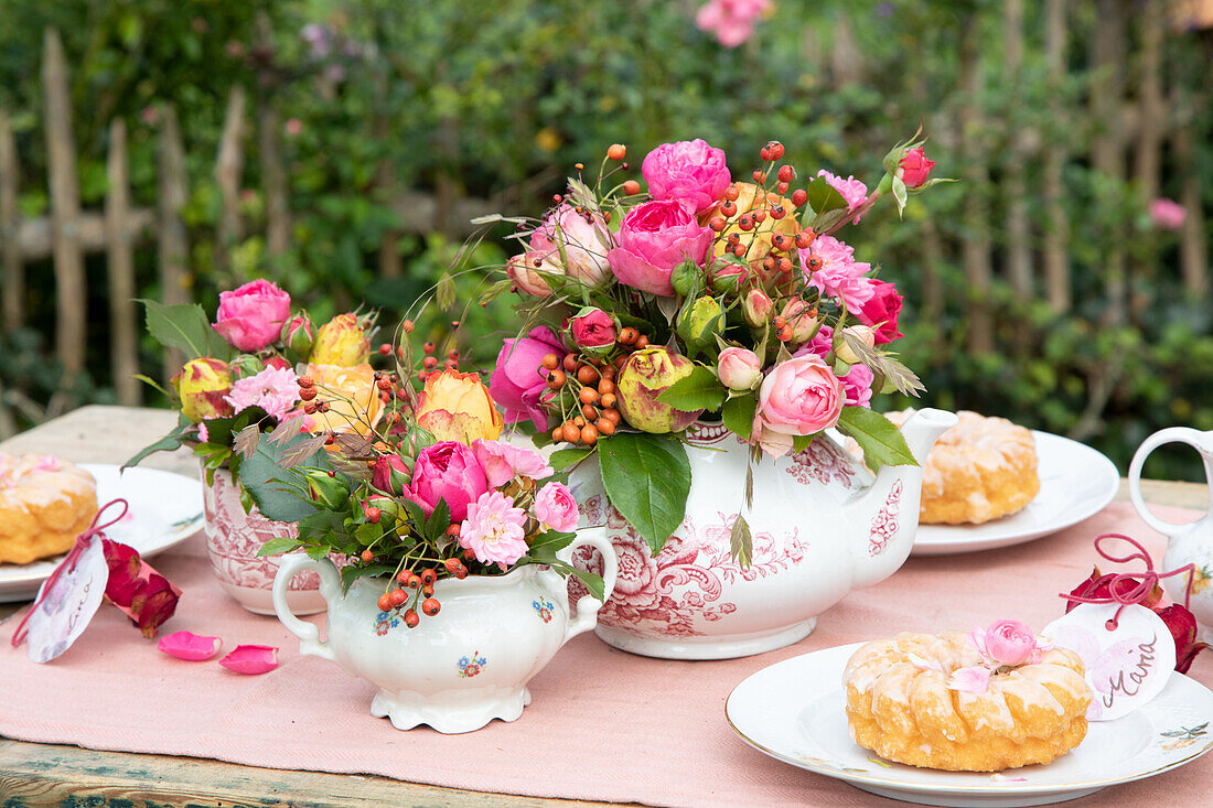 Tea set with bouquets of roses and pastries on garden table in summer